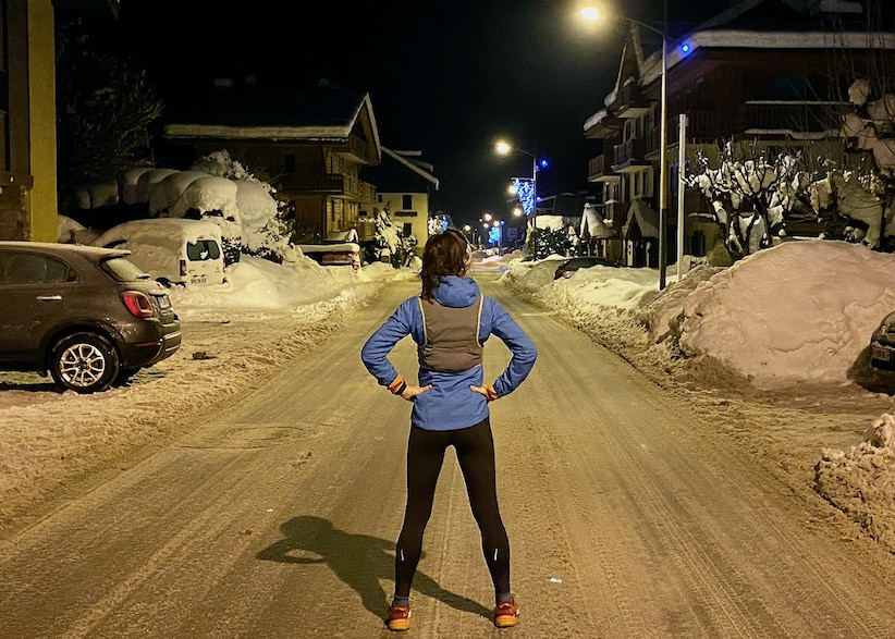 Trail running in the dark. Runner standing in middle of road at night with snow on the ground. 