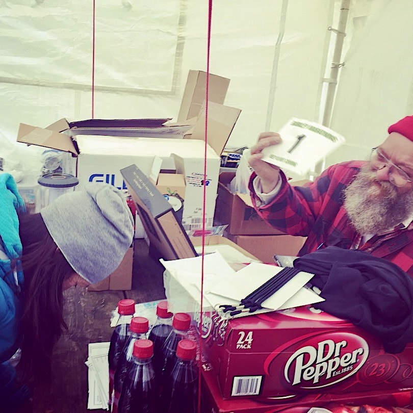 The Barkley Marathons Laz is behind a desk with a list of runners and Dr Pepper drinks and presents Kaz with bib number 1